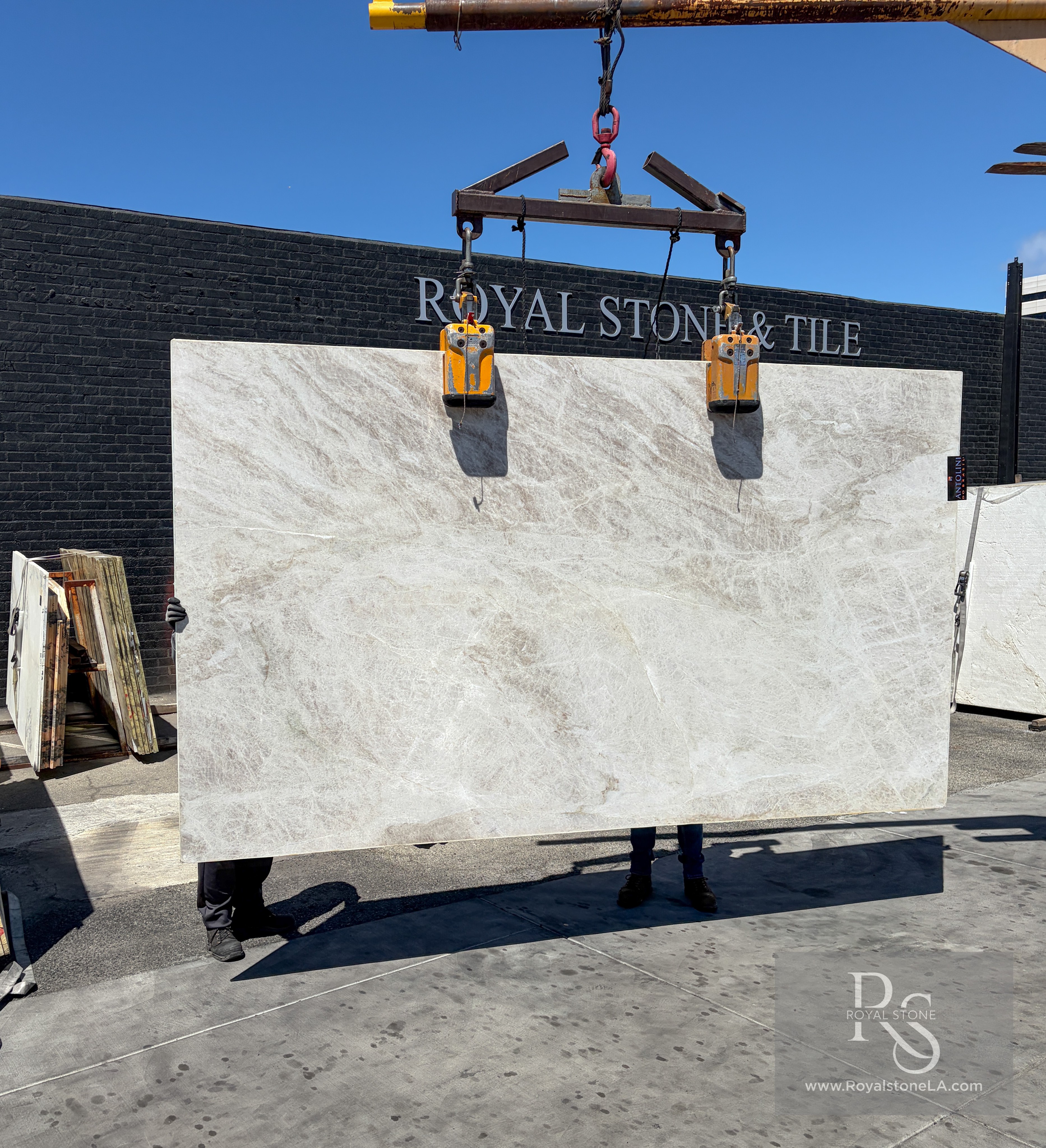 Antolini Taj Mahal Select light-shade quartzite slab, 2cm soft-leathered, 77 by 131 inches, with a pale champagne-ivory field and quiet taupe veining, hanging from a crane at the Royal Stone & Tile Los Angeles yard