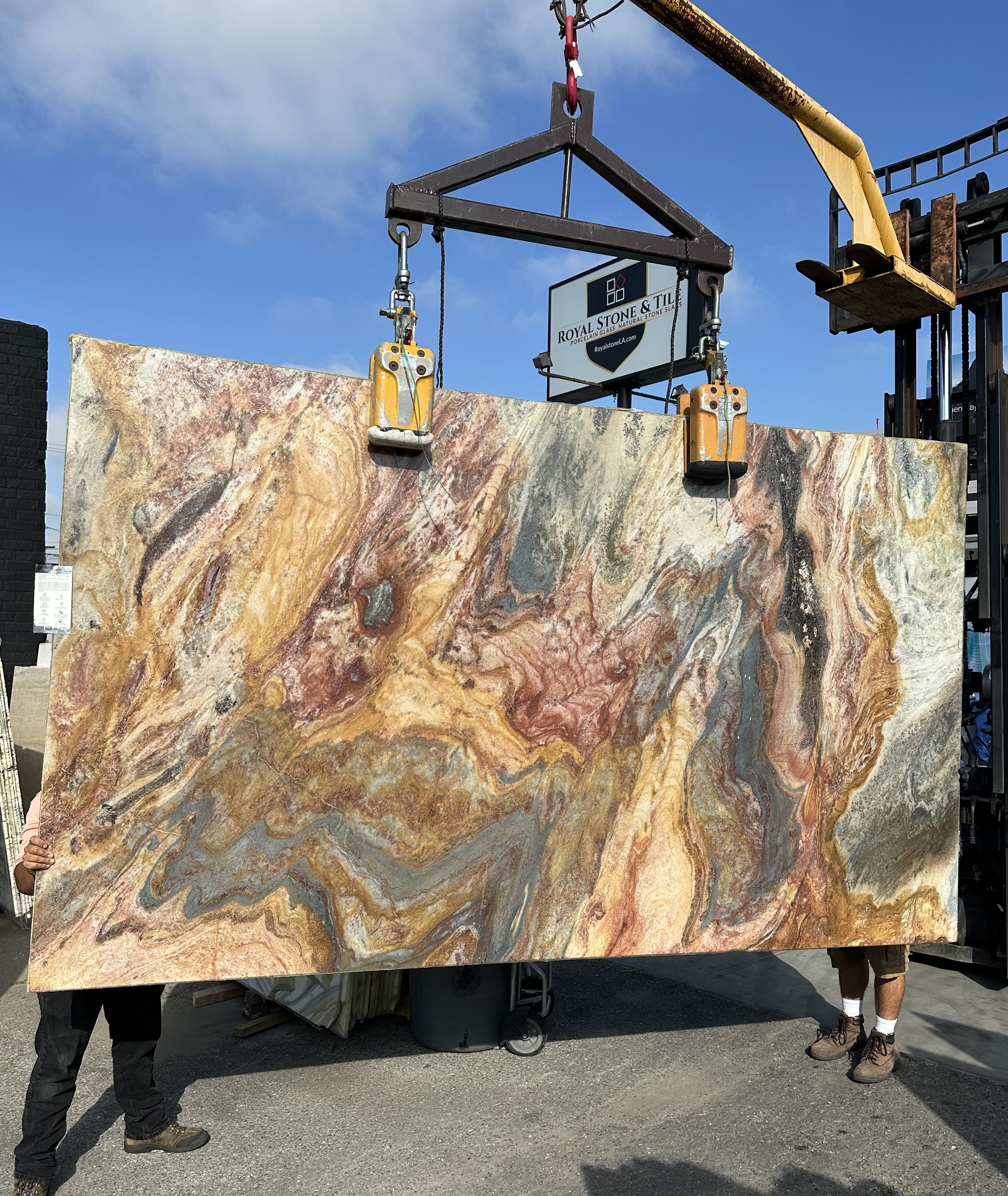 Antolini Van Gogh Blue Louise quartzite slab, 2cm polished, 75 by 128 inches, with painterly swirls of amber, gold, rose, slate-blue, and charcoal across a warm field, hanging from a crane at the Royal Stone & Tile Los Angeles yard