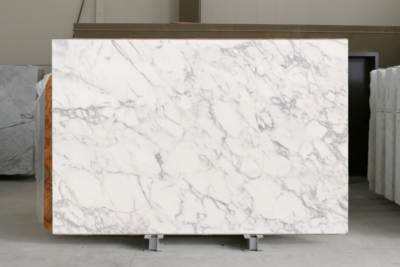 White marble slab with bright white ground and crisp grey veining, photographed standing in the factory