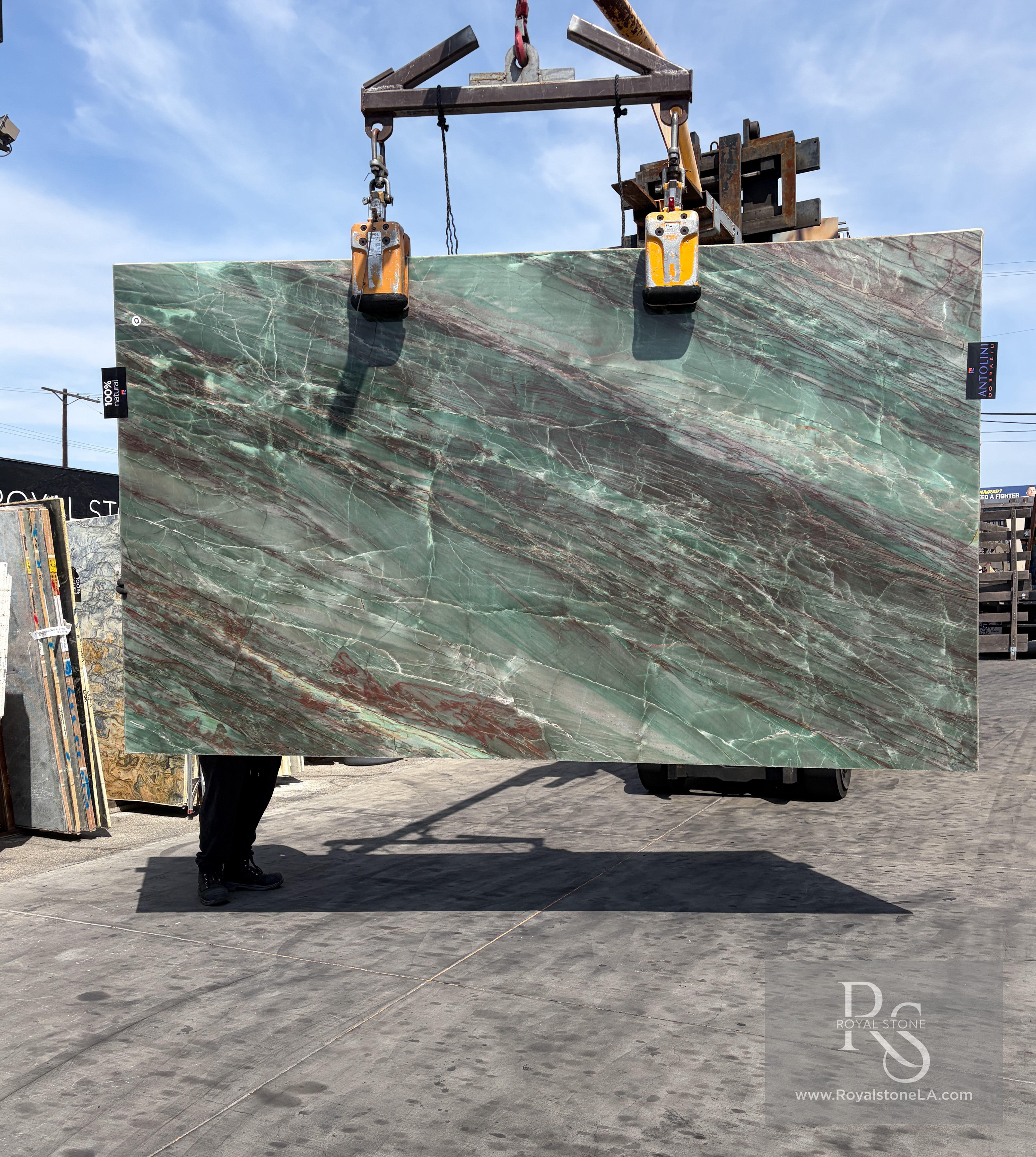 Antolini Thunderflash green quartzite slab, 2cm polished, 76 by 129 inches, with sweeping diagonal red and copper veining across a pale seafoam-green field, hanging from a crane at the Royal Stone & Tile Los Angeles yard